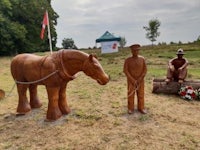 a wooden statue of a man and a horse in a field