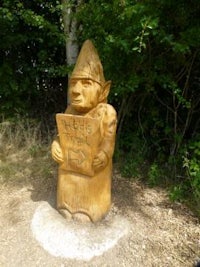 a wooden statue of a gnome holding a sign