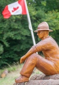 a wooden statue of a man sitting in front of a canadian flag