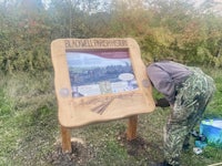 a man is standing next to a wooden sign in the woods