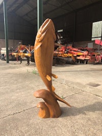 a wooden sculpture of a fish in front of a barn