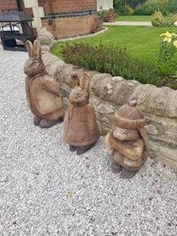 three wooden rabbit statues in front of a stone wall