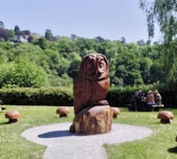 an owl sculpture in a park with people sitting around it