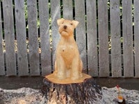 a wooden sculpture of a fox terrier sitting on top of a tree stump