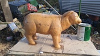 a wooden sculpture of a sheep sitting on top of a piece of wood