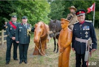 a group of men in uniform standing next to a wooden statue of a horse