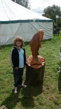 a young boy standing next to a wooden fish sculpture