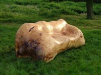 a bench made from a tree stump in the middle of a grassy field