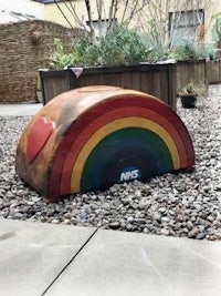 a rainbow sculpture sits on the ground in a garden