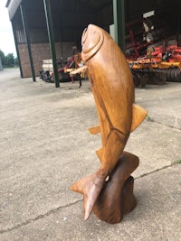 a wooden fish sculpture in front of a barn