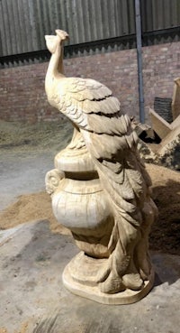 a peacock statue is sitting on top of a piece of wood