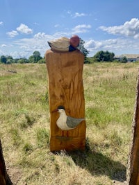 a wooden sculpture with a bird on it in the middle of a field