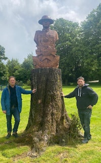 two men standing next to a wooden statue in a park