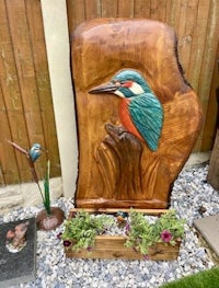 a wood carving of a kingfisher in a garden