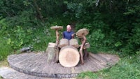 a man posing with a wooden drum set in the woods