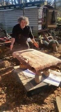 a man standing next to a wooden table in the woods