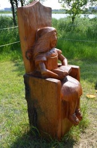 a wooden sculpture of a girl sitting in a chair