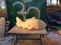 a carved fish sitting on a table in the woods