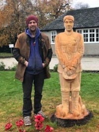 a man standing next to a wooden statue of a soldier