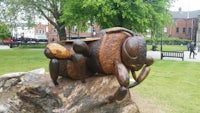 a sculpture of a bee sitting on a log in a park