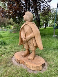 a wooden statue of a boy with a cape